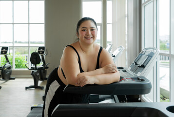 Fototapeta premium A plus-size woman stand on a gym treadmill, resting or preparing to exercise.