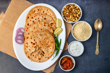 Sattu paratha, a spiced chickpea flour-stuffed flatbread, served hot with tangy pickle and cool, creamy raita for a flavorful meal.
