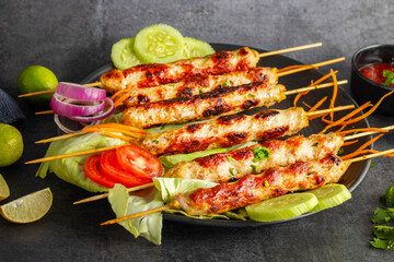 Juicy chicken seekh kababs, grilled to perfection, served with refreshing mint chutney and tangy tomato sauce for a flavorful meal.