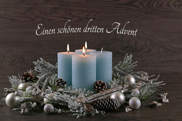 Dekoration zum dritten Advent: Adventskranz mit hellblauen Kerzen, Weihnachtskugeln und dem Text...