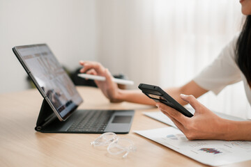 Fototapeta premium Professional woman using smartphone and tablet at a desk, showcasing multitasking in a modern office environment.
