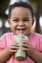 Cheerful plus-size child drinking a green smoothie with a straw