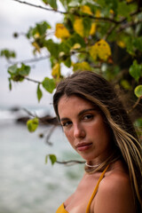 A beautiful portrait showcasing a young woman standing by the ocean amidst tropical foliage