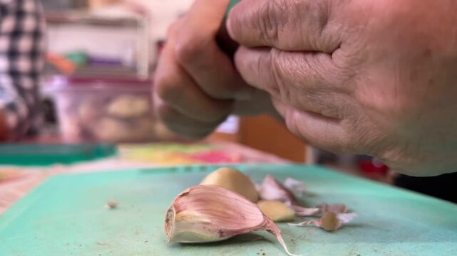 A person peels garlic on a kitchen cutting board for a cooking preparation close-up shot