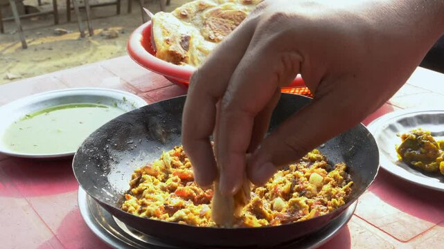 At a charming local dhaba, people relish a delightful breakfast featuring warm, crispy parathas served alongside a flavorful omelet, tangy pickle, and refreshing raita.