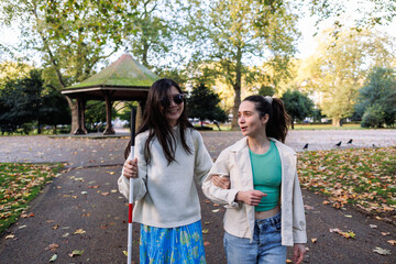 Young woman helping blind friend walking in the park