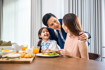 Happy Asian family enjoying a meal together at a table, father wearing a suit, mother and daughter having breakfast in morning at home, Parents laughing with their children, support and healthy meal