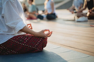 A woman is comfortably sitting in a classic lotus position on her colorful yoga mat, practicing her...