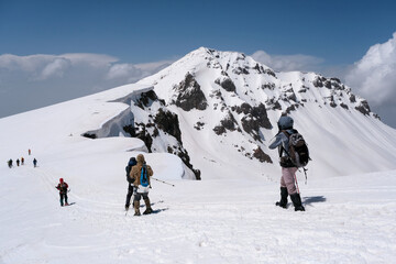 Group of tourists on the background of West Summit of Mount Aragats cowered with snow on sunny spring day. Armenia.