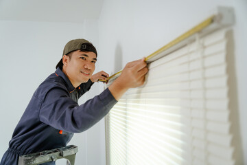 Asian technician carefully measuring for custom blinds installation in a sleek office, using professional tools, modern interior, precise and clean setup.