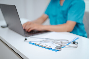 Close-up of doctor's hands on laptop keyboard with stethoscope nearby, capturing the focus and detail of merging technology with medicine.