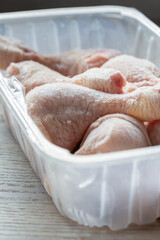 Frozen chicken drumsticks in a plastic container defrosting. On a wooden chopping board