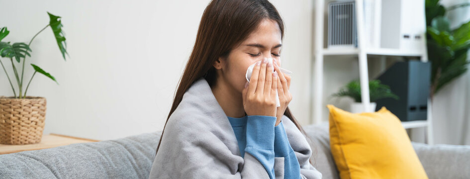 Sick in winter season common cold disease concept, Young woman have a runny nose and flu using tissue to blow her nose on the sofa during winter.