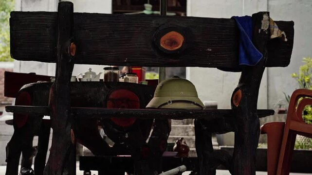 Rustic outdoor tea setup in Vietnam, featuring a green pith helmet on a wooden bench, with a teapot, jars, and a pot of roll tobacco on a wooden table. vintage, tranquil atmosphere with natural wooden