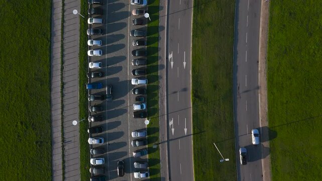parking lot full of cars with parallel road with lane for cars, free grass separating both, top aerial drone view