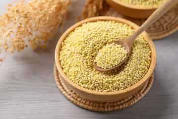 Organic yellow millet grain in wooden bowl with spoon on white table, Healthy food ingredient