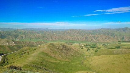 Fototapeta premium Expansive view of rolling green hills under a vibrant blue sky.