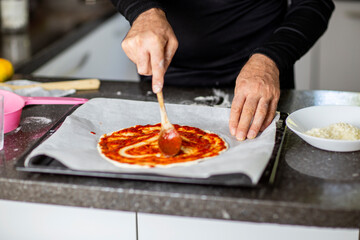 Person adding tomato sauce to pizza heart shaped