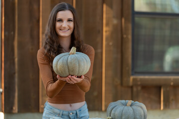 Fototapeta premium Woman holding a pumpkin at a rustic farm setting.