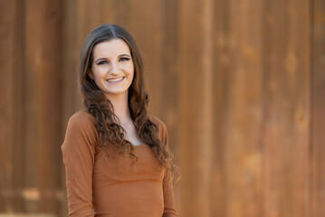 Smiling woman posing against rustic wooden background in fall attire.