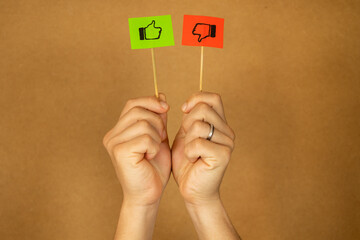 Male hand holding two flags with like and dislike symbols on red and green pieces of paper on a...