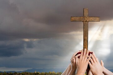 Human hands praying with Christian cross at sunrise