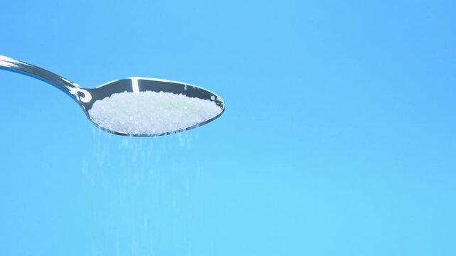 Slow motion video of sugar crystals falling out of metal spoon