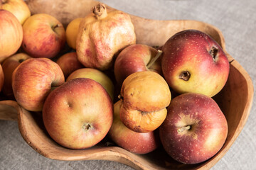 Organic apples and pomegranate in wooden bowl on gray background. Autumn harvest. Still life.