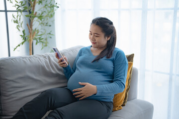 Pregnant asian woman holding smartphone at home using mobile app for pregnant women Positive life moment in pregnancy time