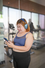 Female with smart phone after workout at Gym. Obese asian woman watching online workout training class.