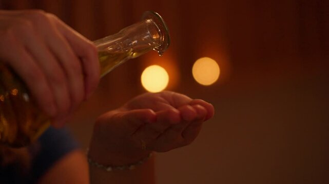 Close-up of hands pouring aromatic massage oil from a glass bottle into the palm, with warm golden lighting and soft bokeh in the background. Concept of relaxation and self-care.