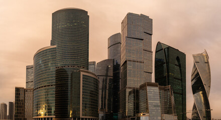 Skyscrapers in business district against blue sky. Looking Up high-rise office buildings. Evening time, sunset. Orange, yellow and gold shades of color. Angled view.