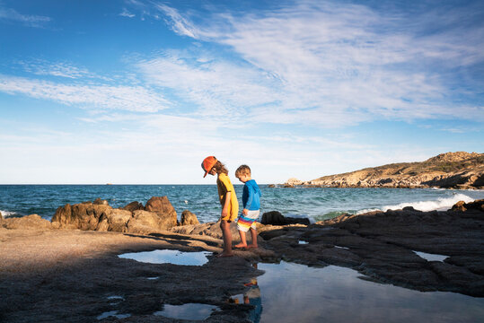 A boy and girl look into tide pools on desert beach