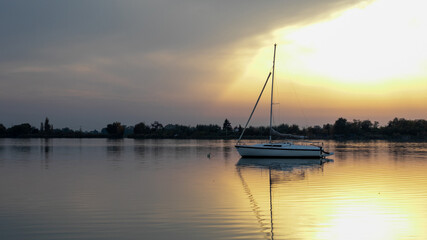 A serene sailboat is reflected in calm waters at sunset, capturing tranquility and adventure, ideal for summer leisure