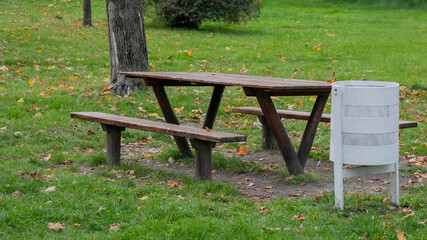 Wooden picnic table with benches and a white trash can on green grass, related to environmental awareness and outdoor gatherings