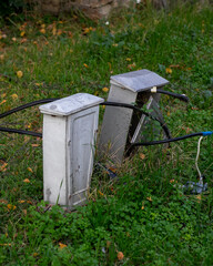 Two neglected utility boxes with exposed cables in overgrown grass, representing urban decay and potential electrical hazards