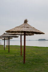 Wooden beach parasols on a grassy lakeshore under overcast skies evoke summer retreat and peaceful vacation vibes