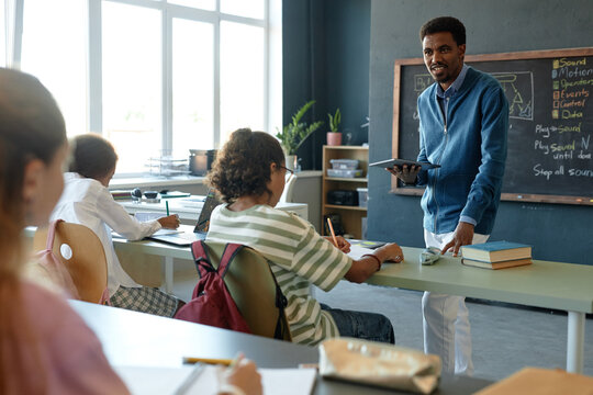 At angle view of school classroom with group of children sitting in row and African American teacher explaining topics copy space