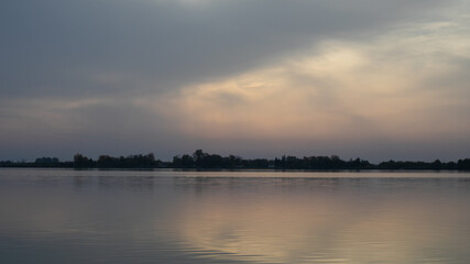 Tranquil sunset over a serene lake with distant trees, evoking relaxation and contemplation,...