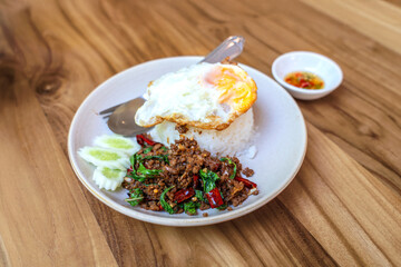 Thai basil minced beef (Pad Gra Prow) with fried egg on steamed rice in a white plate and chili in fish sauce in small cup on a wooden table in a restaurant Street food Cafe style.