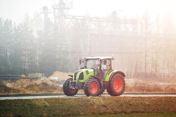 Modern green tractor driving on rural foggy road