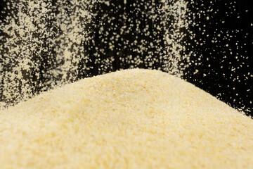 Uncooked dry semolina pour on a black background
