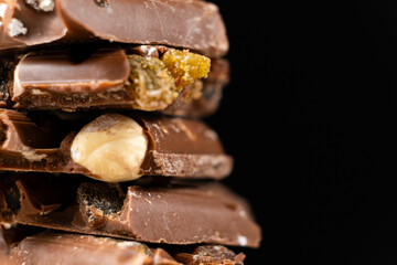 Pieces of broken milk chocolate with nuts and raisins on a black background copy the space.