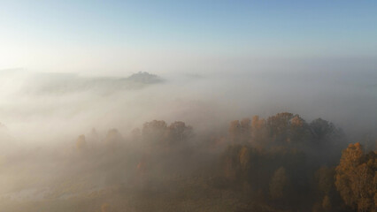 Aerial view of morning fog covering autumn forest and fields at sunrise