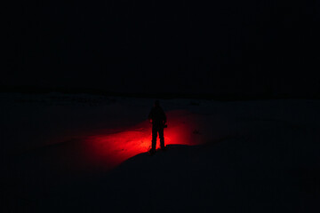 A Person in the Snow Shining a Red Flashlight in the Dark