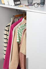 White wardrobe full of clothes and different accessories on it. Home interior and organization of stuff. Woman capsule clothing hanging in the closet