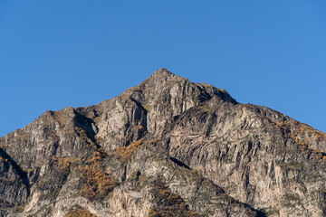 Kabardino-Balkaria. El-Tyubu. Rocky mountains with trees growing on their slopes glow in morning sun. Close-up. Chegem Gorge. Unique rocky ridge with steep cliffs against blue autumn sky.