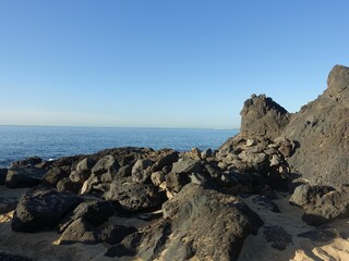 Rocky coastline with black volcanic rocks and calm ocean.