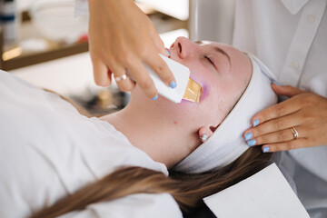 A professional skincare specialist applies a cooling gel on a client's face with a gentle spatula, focusing on precise treatment.