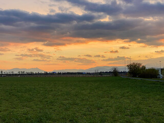 A stunning sunset with orange and pink hues illuminating the sky over a mountainous horizon, creating a dramatic silhouette with scattered clouds.